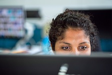 Eine Frau Blickt über den Bildschirm eines Computers hinweg. Es sind nur ihre Augen und ihre Haare zu sehen.